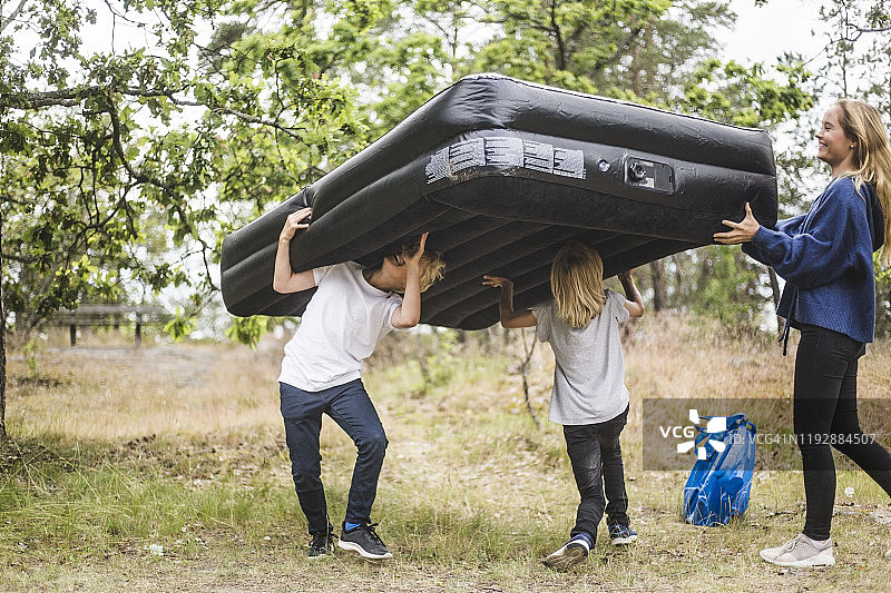 在露营地和兄弟姐妹一起抬着充气床垫的少女全身照图片素材