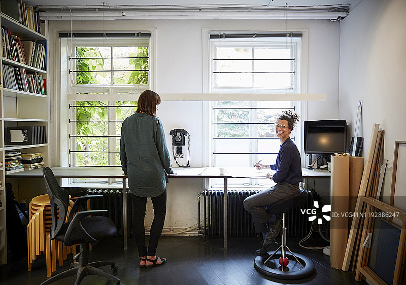 微笑的女建筑师与同事在办公室的桌旁图片素材