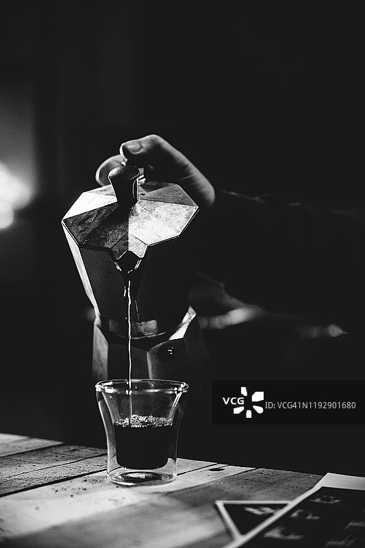 黑白阴沉的咖啡师场景，男人手持滤压壶向咖啡杯中倒咖啡图片素材