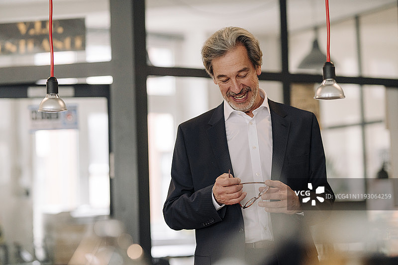 在办公室里拿着眼镜的快乐年长商人图片素材