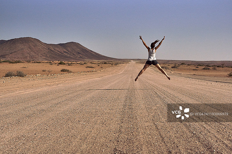 在纳米比亚达马拉兰土路中央跳跃的女人图片素材