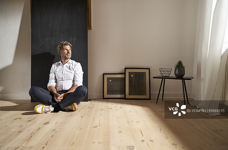 坐在家里地板上看着远方的放松的成熟男人肖像图片素材