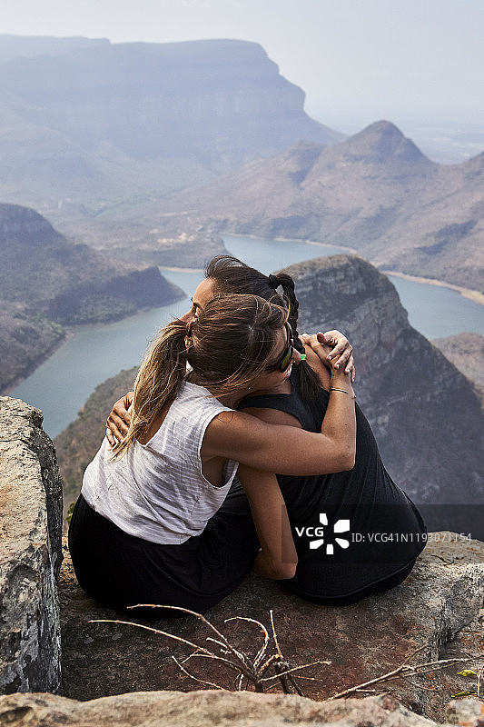 两名女子在岩石上拥抱，背景是美丽的风景，南非布莱德河峡谷图片素材