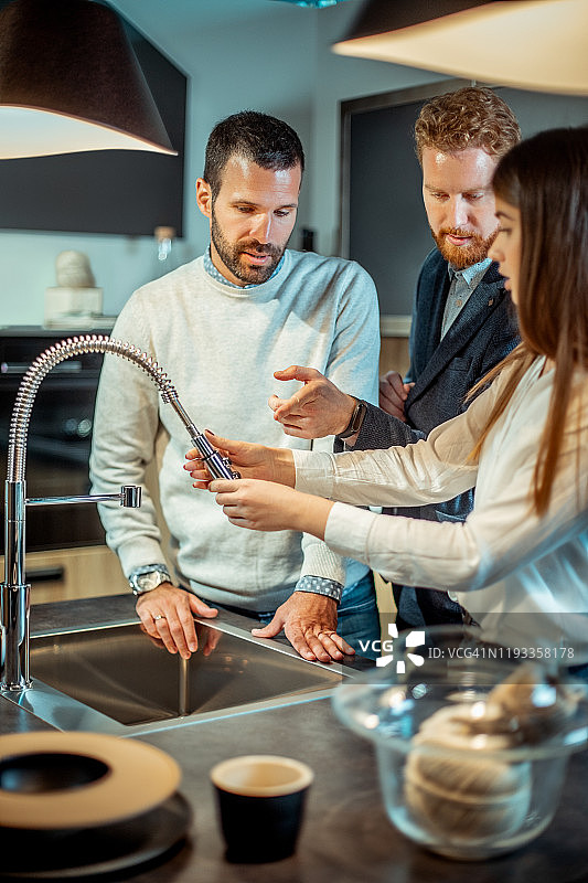 年轻夫妇在商店选购厨房软管，售货员提供帮助图片素材