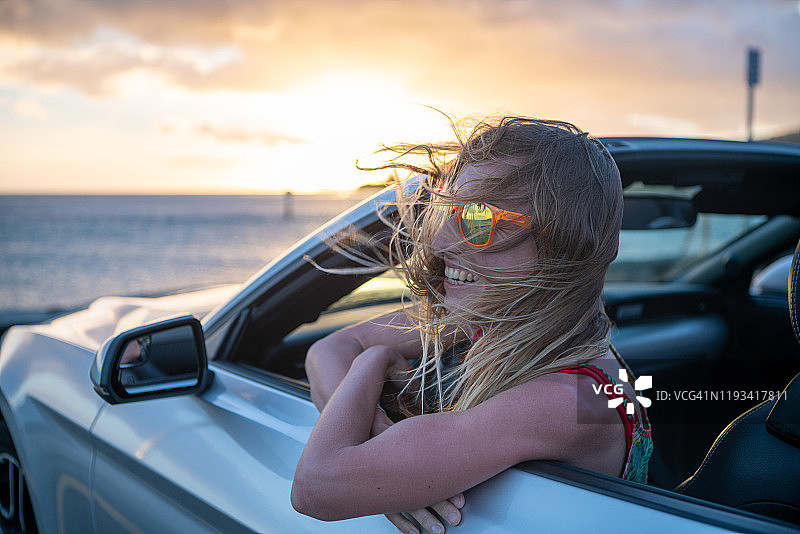 在敞篷车里沉思日落海景的金发女人图片素材