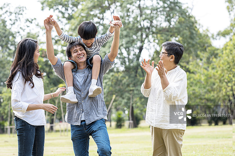 亚洲家庭周末假日亲子时光：父亲背着孩子在公园里玩耍图片素材