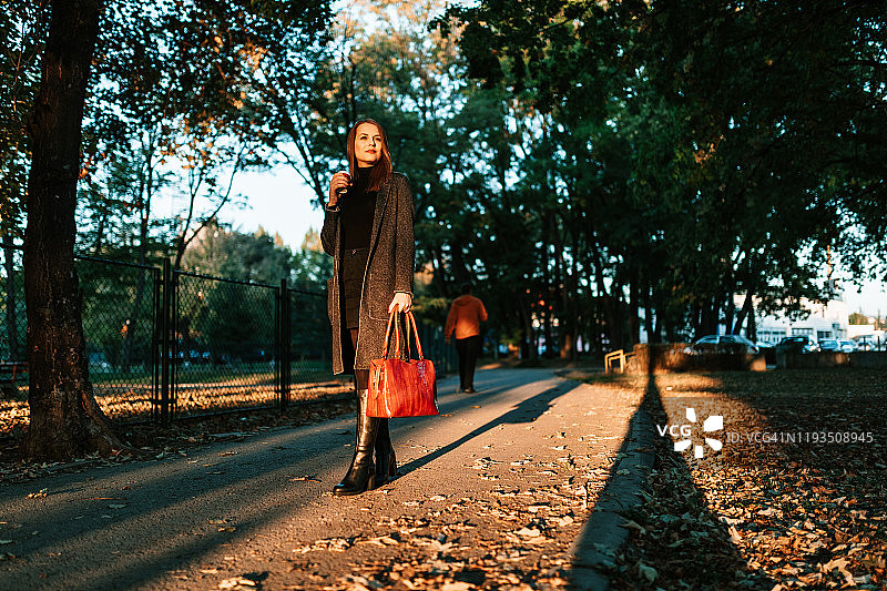 在阳光明媚的日子里，端着咖啡杯在公园里散步的女人图片素材