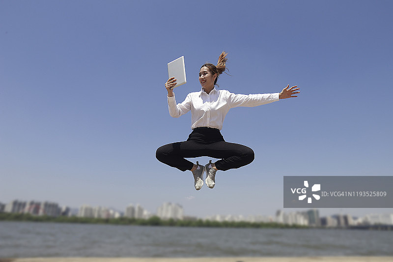 跳跃的女商人，手持平板电脑图片素材