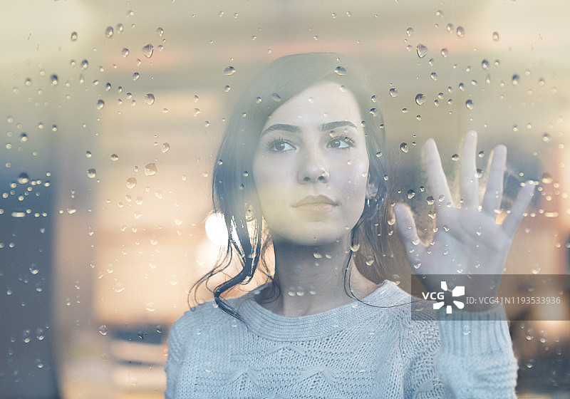 望着带雨滴窗户的沉思年轻女子图片素材