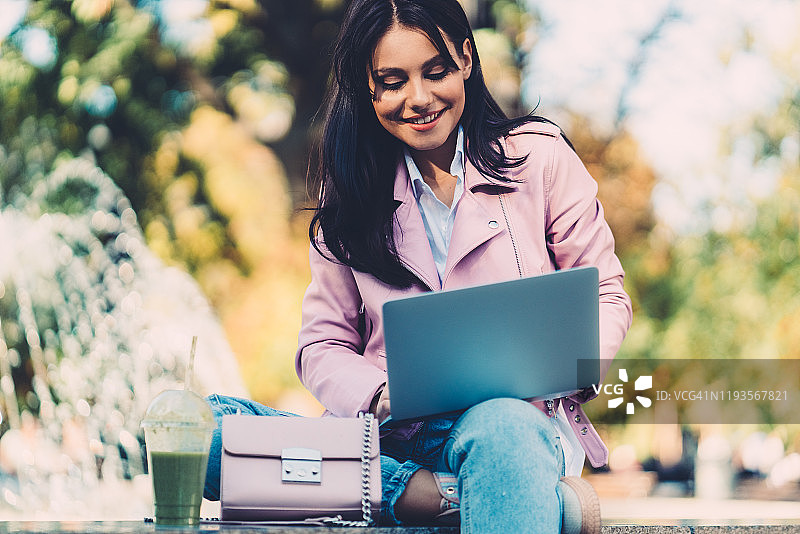 年轻学生坐在喷泉旁使用笔记本电脑图片素材