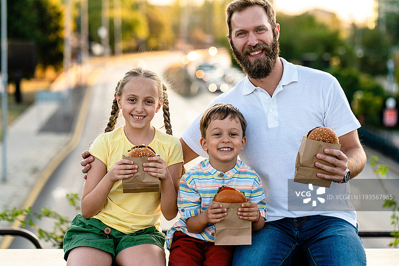 父亲和两个孩子在城市里吃快餐图片素材