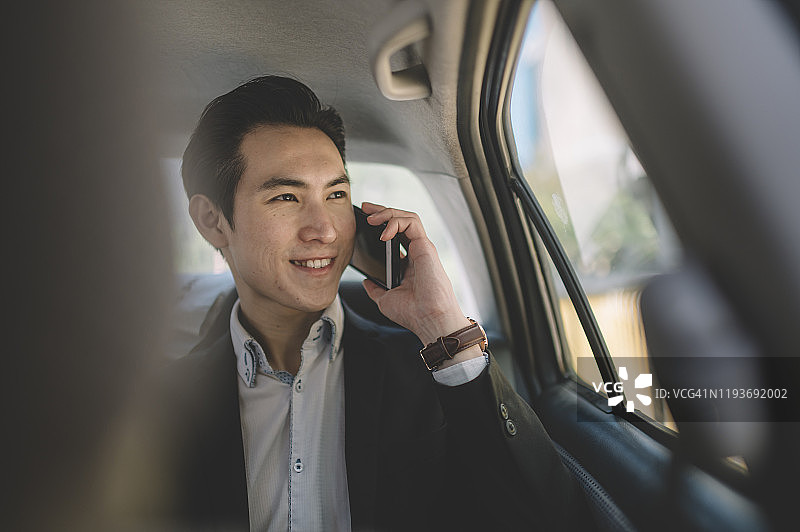 坐在汽车后座与商业伙伴通电话的亚洲华人商人图片素材