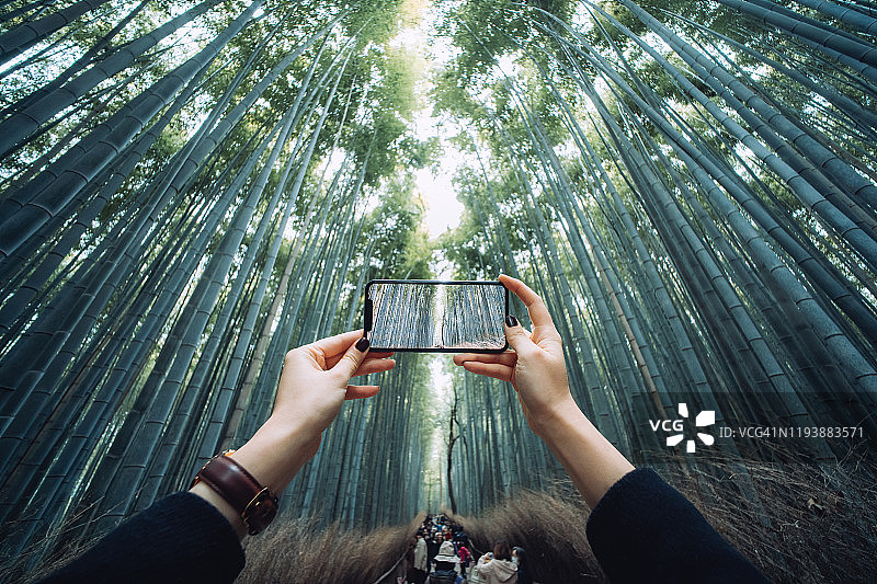 在日本京都岚山竹林用智能手机拍摄壮丽景色的亚洲女性游客图片素材