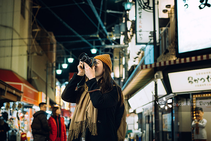 微笑的年轻亚洲女游客在大阪繁忙的当地街道上用相机拍照图片素材