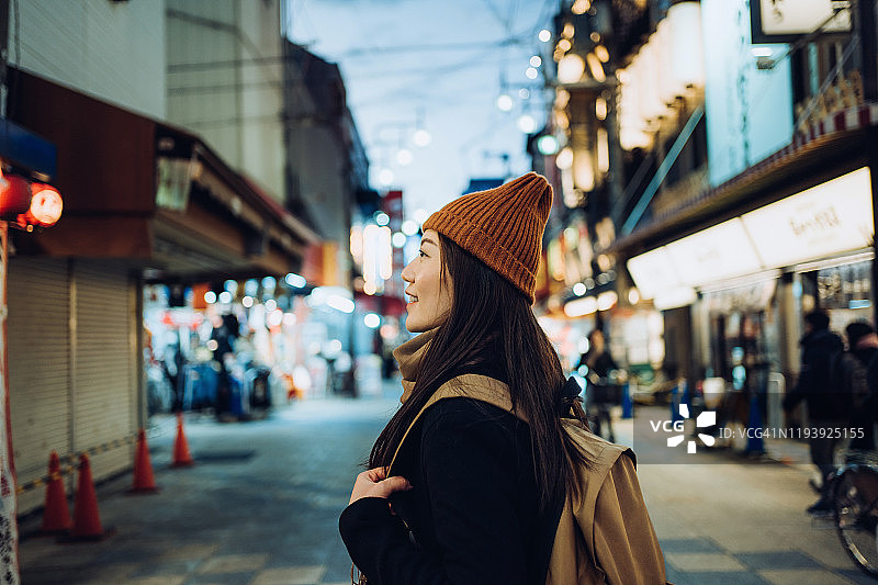 微笑的年轻亚洲女性旅行者在日本大阪繁华的当地城市街道上探索和漫步图片素材