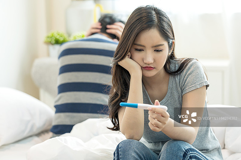 年轻亚洲夫妇卧室，女子怀孕检测呈阳性，感到悲伤和恐惧图片素材
