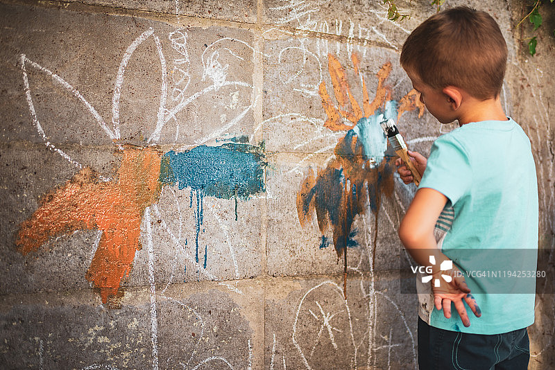 快乐的小男孩在墙上开心地涂鸦。图片素材