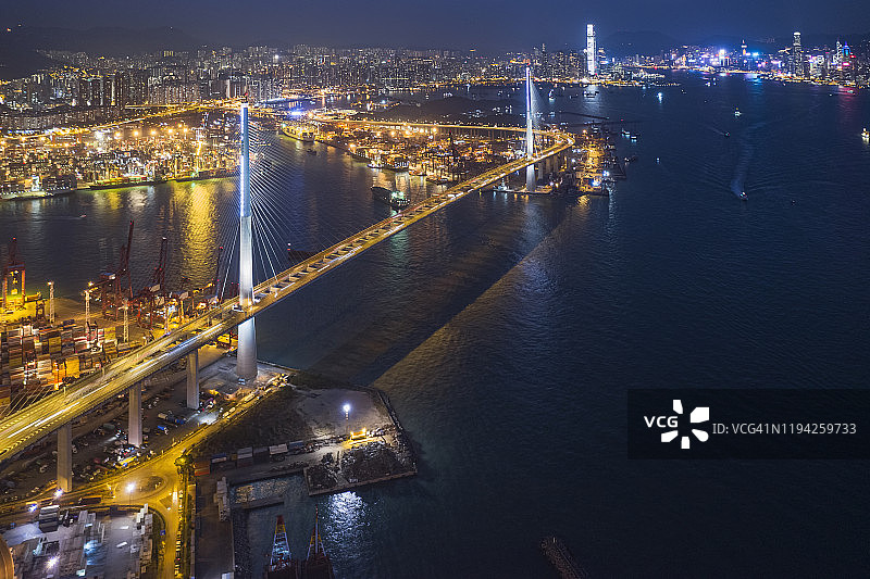 商业港口码头和起重机桥梁装载集装箱，以城市景观为背景，用于商业物流、进出口、航运或运输的航拍景色图片素材