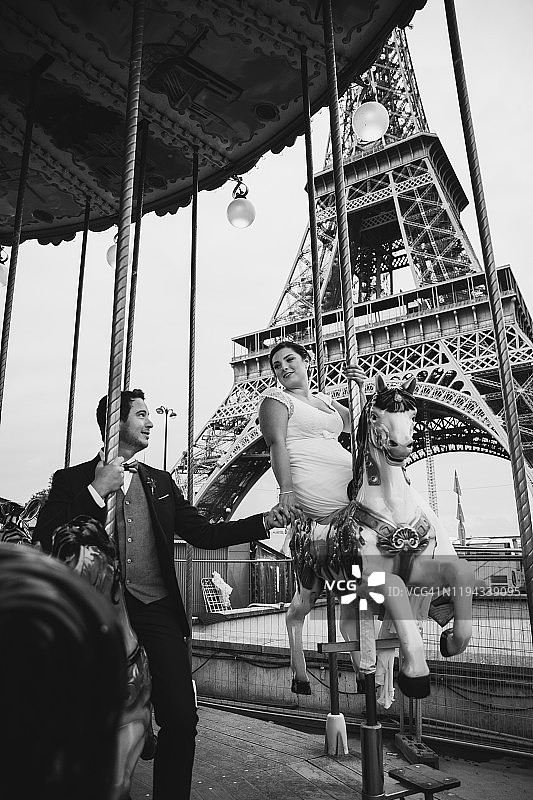 在巴黎旋转木马上玩耍的新婚白人年轻夫妇图片素材