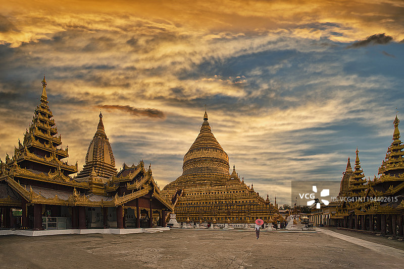 日落时分，缅甸女子撑红伞走过瑞西光塔图片素材