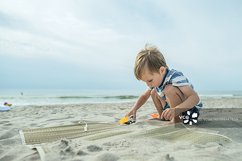 可爱的小男孩在沙滩上玩玩具车图片素材