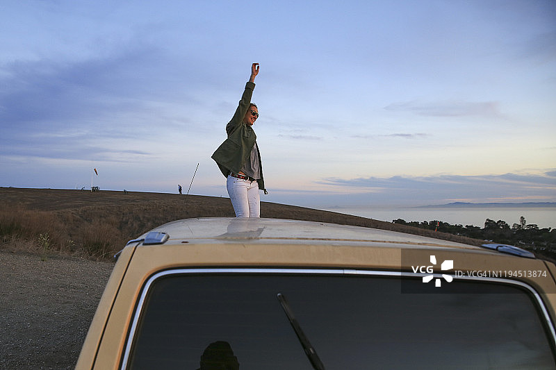 在汽车引擎盖上跳舞的自由奔放的年轻女孩图片素材