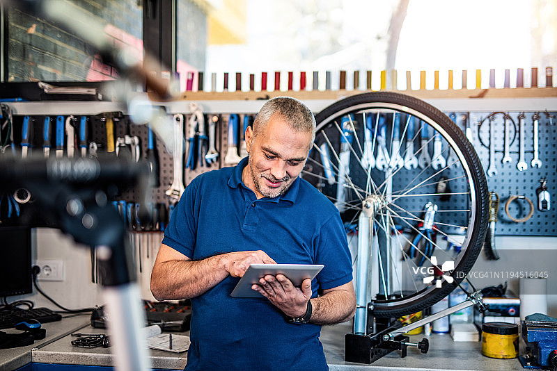 快乐的自行车修理工用平板电脑搜索零件图片素材