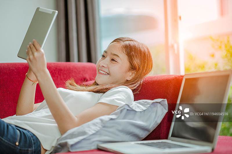 躺在沙发上，拿着平板电脑和笔记本电脑的快乐年轻女人图片素材