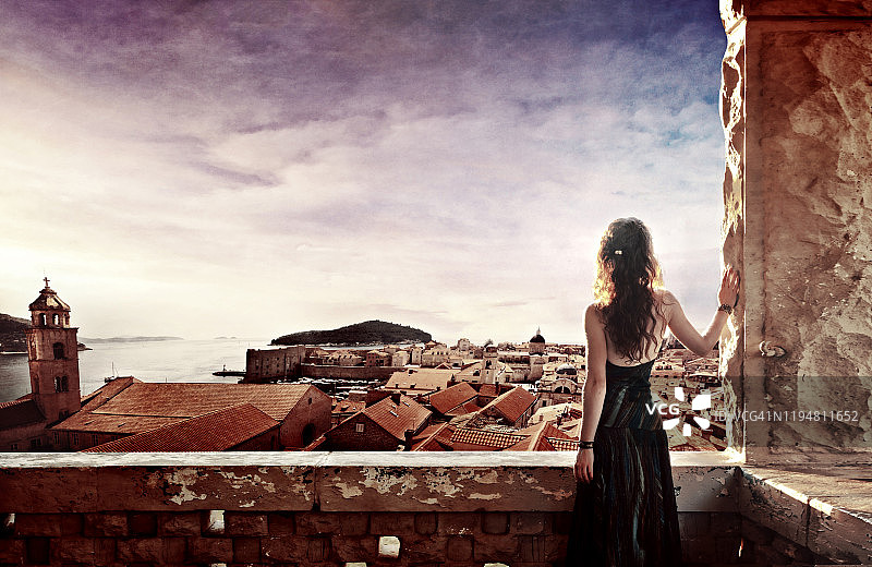 红发女子靠在城堡墙上的背影，背景是克罗地亚杜布罗夫尼克老城的城垛图片素材
