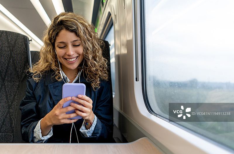 快乐的女人在火车上用手机发短信听音乐。图片素材
