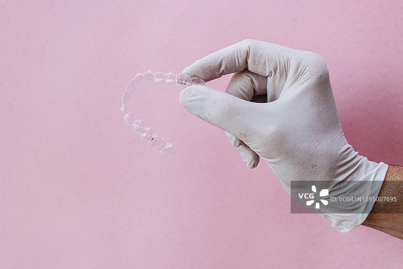 医生手持粉色背景的透明牙齿矫正器图片素材