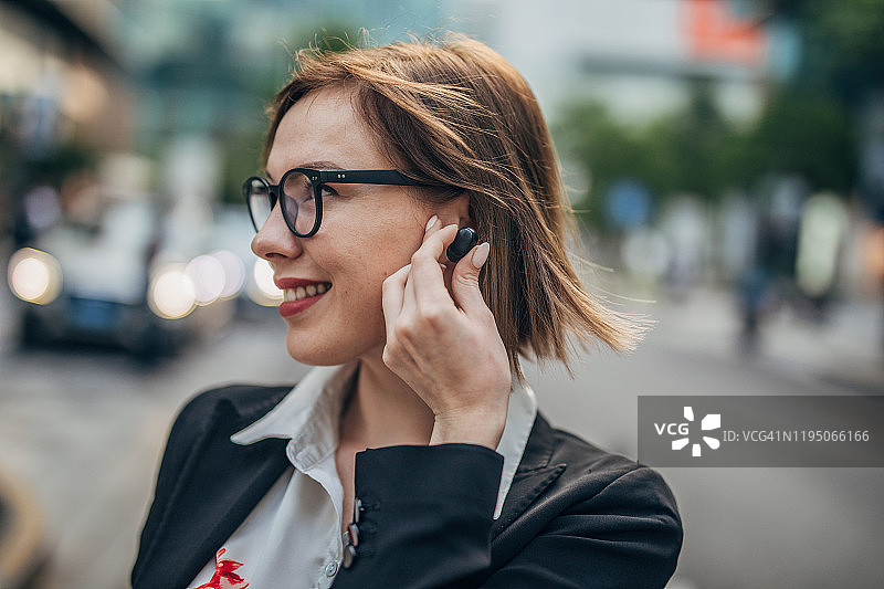 戴着无线耳机的年轻现代商务女士在街上图片素材