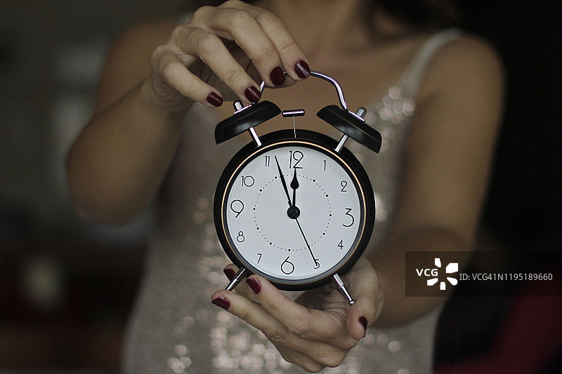 拿着12点老式闹钟的女人：新年概念图片素材