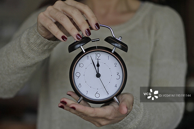 女人拿着12点的老式闹钟图片素材