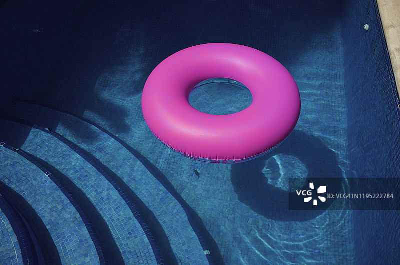 阳光明媚的蓝色游泳池中的亮粉色充气圈图片素材