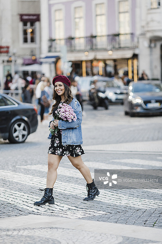 微笑的年轻女子手捧鲜花穿过街道肖像图片素材