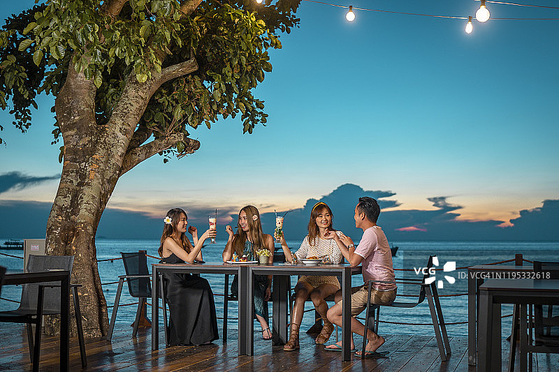 三位年轻的中国亚洲女性和一位年轻的中国亚洲男子在海边餐厅用餐图片素材