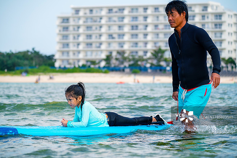 在热带度假期间，父亲在海中与小女儿在冲浪板上玩耍图片素材