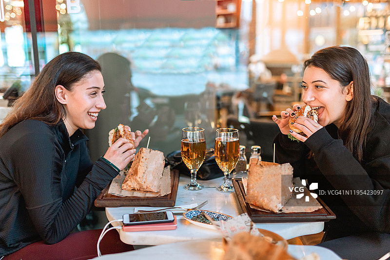 年轻夫妇和朋友在餐厅享用小吃和饮料，吃汉堡薯条喝啤酒图片素材