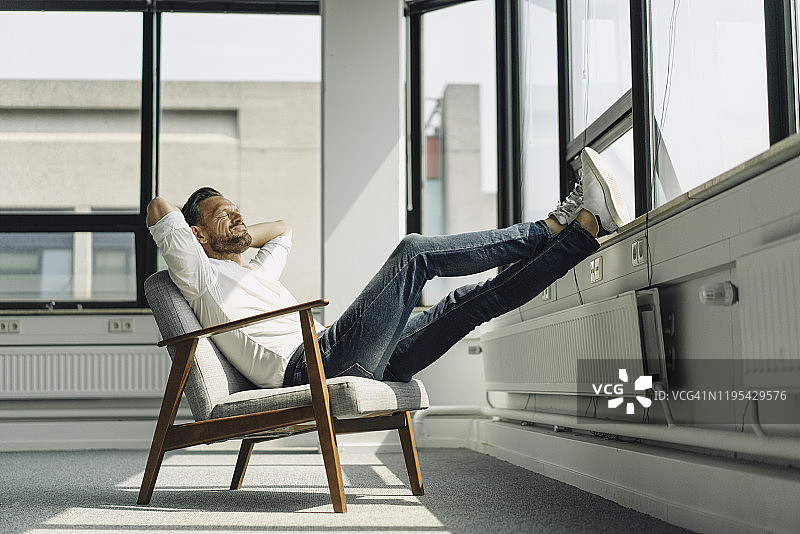 在空荡荡的办公室里靠窗放松的中年商人图片素材