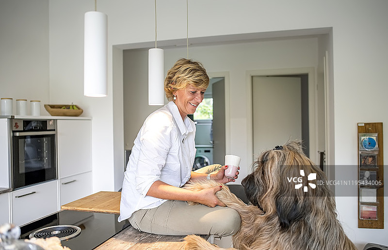 在家中厨房里带着狗的微笑女人图片素材