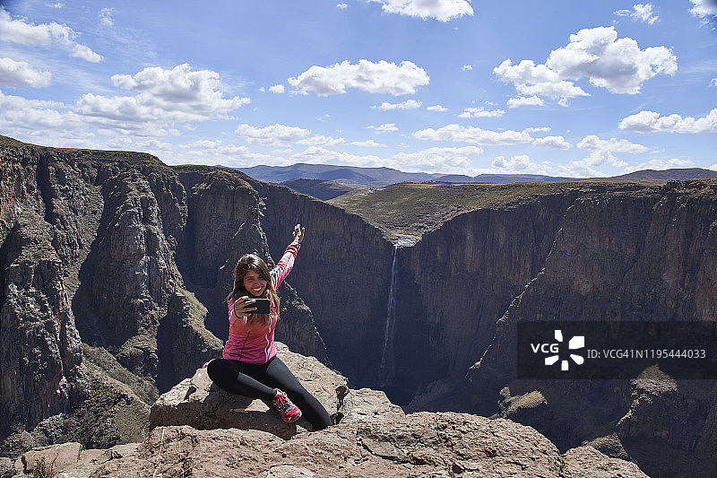 快乐的女人坐在莱索托Maletsunyane瀑布的山顶上自拍图片素材