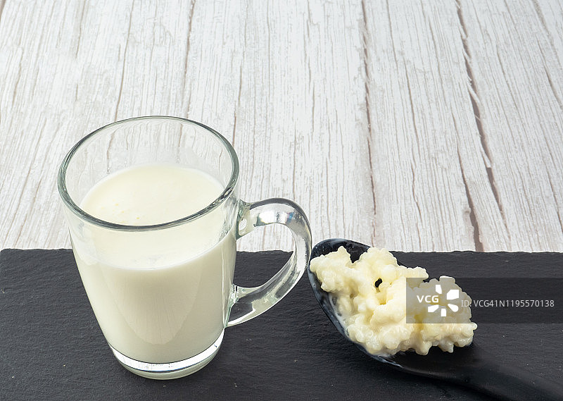 塑料勺中的开菲尔菌和玻璃杯中的全牛奶图片素材