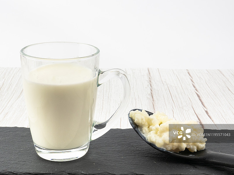 塑料勺中的开菲尔菌和玻璃杯中的全牛奶图片素材