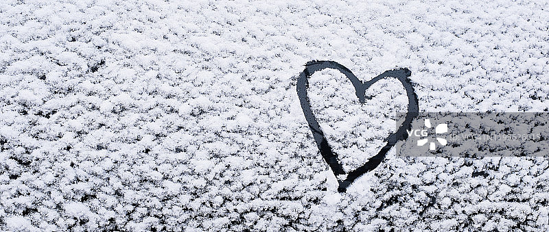 车玻璃上画着的心，以雪为背景。爱、浪漫、情人节的象征。图片素材
