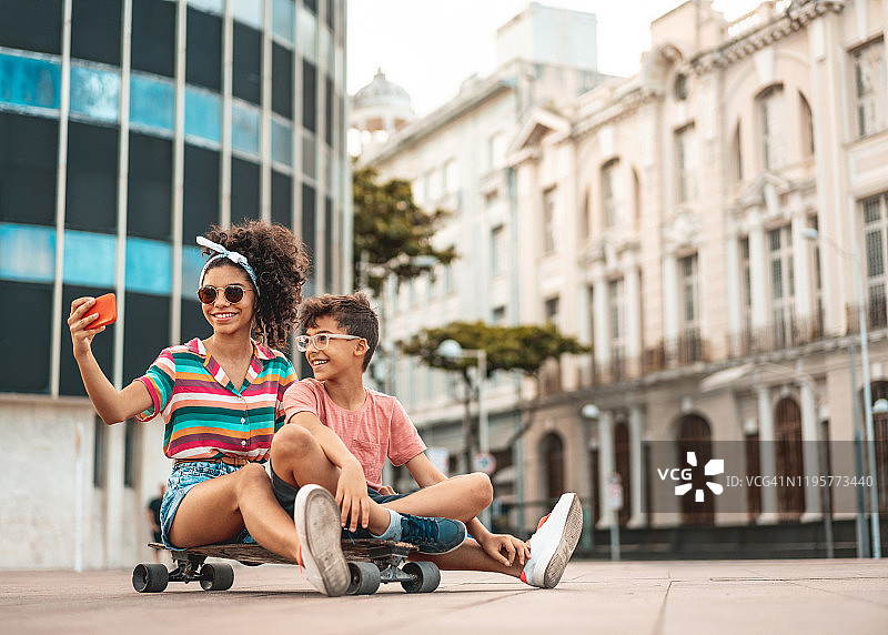 兄弟姐妹坐在长板上在户外自拍图片素材