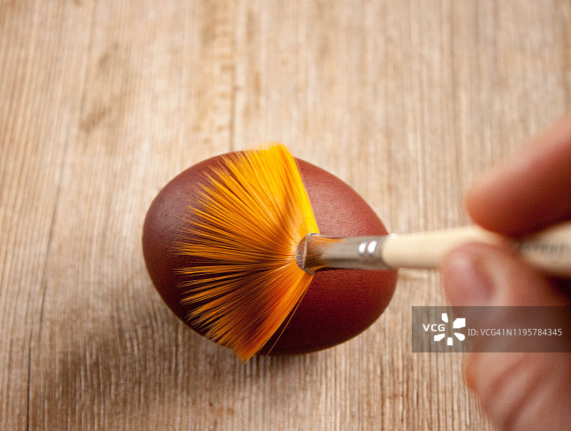 人手用刷子绘制复活节彩蛋，俯视图，木质背景，复活节概念图片素材