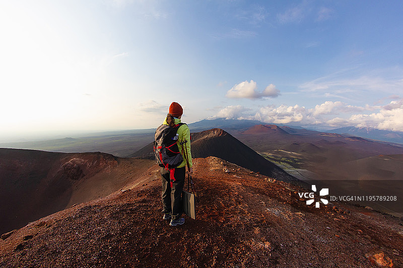 年轻女孩在云雾缭绕的火山背景下徒步旅行，背着背包图片素材
