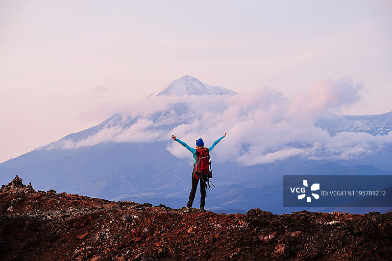 年轻女孩在云雾缭绕的火山背景下徒步旅行，背着背包图片素材