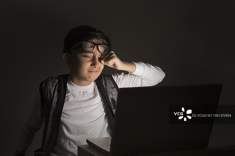 看着笔记本电脑揉眼睛的年轻男孩（儿童）图片素材